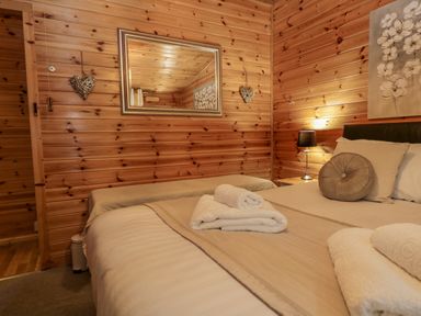 A bedroom with a bed and a bench next to a wooden wall with a mirror and decorative items at Scafell Lodge Skiptory Howe 7 White Cross Bay Holiday Park near Windermere