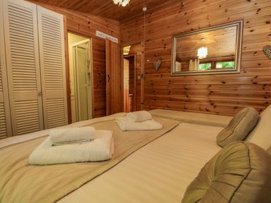 A bedroom with a bed with towels on it wooden walls a mirror and a wardrobe at Scafell Lodge Skiptory Howe 7 White Cross Bay Holiday Park near Windermere