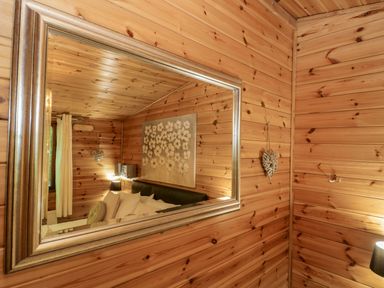 A wooden paneled room with a large framed mirror reflecting a bed with pillows and floral artwork at Scafell Lodge in Skiptory Howe 7 White Cross Bay Holiday Park near Windermere