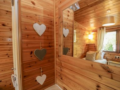 A bedroom with wooden walls a bed with pillows a window with curtains and hanging heart decorations at Scafell Lodge Skiptory Howe 7 White Cross Bay Holiday Park near Windermere