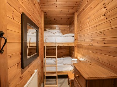A small wooden room with bunk beds a ladder a dresser a lamp a mirror and a table at Scafell Lodge in Skiptory Howe 7 White Cross Bay Holiday Park near Windermere