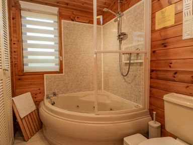 A bathroom with a corner bathtub shower combination wooden walls and a toilet at Scafell Lodge in Skiptory Howe 7 White Cross Bay Holiday Park near Windermere