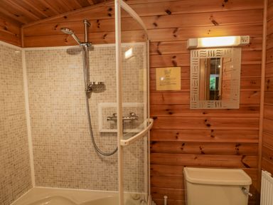 A bathroom with a shower head and tiled walls next to a toilet and a mirror with a light above at Scafell Lodge Skiptory Howe 7 White Cross Bay Holiday Park near Windermere
