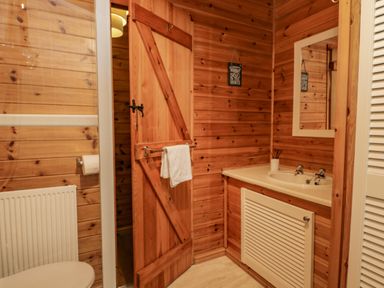 A bathroom with wooden walls a sink with mirror a wooden door and a toilet at Scafell Lodge in Skiptory Howe 7 White Cross Bay Holiday Park near Windermere