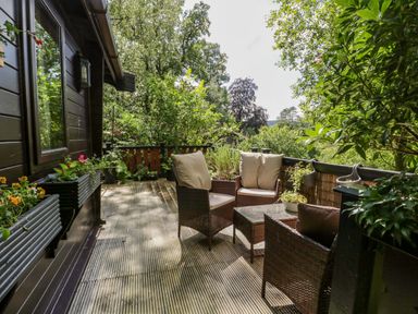 An outdoor patio with wicker chairs and a table surrounded by plants at Scafell Lodge Skiptory Howe 7 White Cross Bay Holiday Park near Windermere