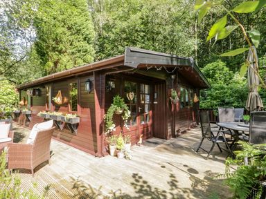 A wooden cabin with flower pots and outdoor furniture on a deck surrounded by trees at Scafell Lodge Skiptory Howe 7 White Cross Bay Holiday Park near Windermere