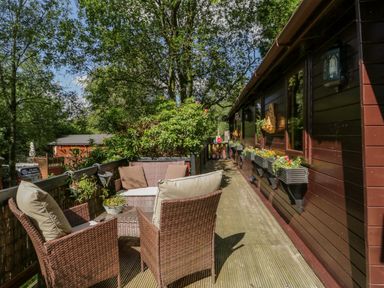An outdoor deck with wicker furniture and flower boxes on the side of a wooden building at Scafell Lodge Skiptory Howe 7 White Cross Bay Holiday Park near Windermere