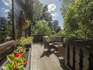 An outdoor wooden deck with cushioned wicker chairs and tables surrounded by plants at Scafell Lodge Skiptory Howe 7 White Cross Bay Holiday Park near Windermere