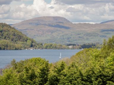 A lake with a sailboat surrounded by trees and hills in the background at Scafell Lodge Skiptory Howe 7 White Cross Bay Holiday Park near Windermere