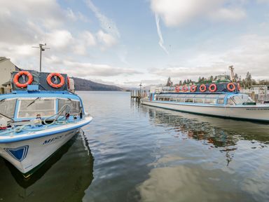 Two passenger boats docked on a lake with hills and a partly cloudy sky in the background