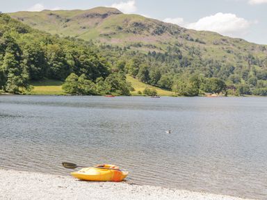 A yellow kayak with paddle on a pebbled lakeshore with hills and trees across the water at Scafell Lodge Skiptory Howe 7 White Cross Bay Holiday Park near Windermere