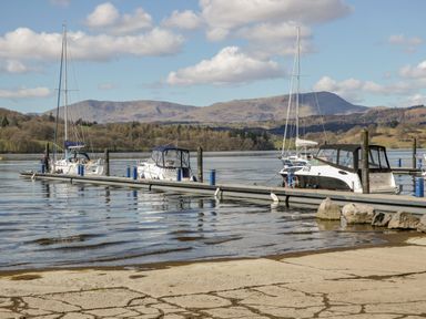 A dock with boats tied up on a lake with mountains and trees in the background at Scafell Lodge Skiptory Howe 7 White Cross Bay Holiday Park near Windermere