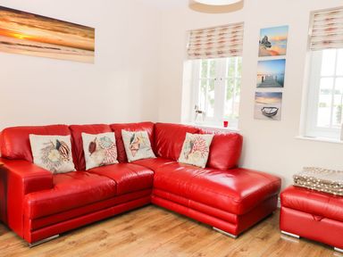 A living room with a red leather sectional sofa and marine-themed cushions at Meadow View in Filey
