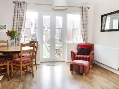 A dining area with wooden table and chairs a red striped armchair with matching footstool and a large window at Meadow View in Filey