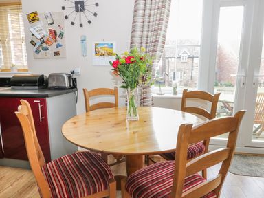 A dining area with a round wooden table and four chairs with striped cushions and a vase with flowers at Meadow View in Filey