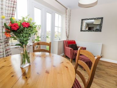 A dining area with a wooden table and chairs a vase with flowers a striped armchair and a wall mirror at Meadow View in Filey