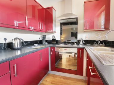 A kitchen with red cabinets a gas stove a stainless steel sink and wooden floor at Meadow View in Filey