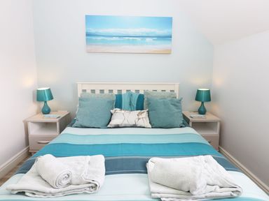 A bedroom with a bed with blue striped bedding and pillows and two bedside tables with teal lamps at Meadow View in Filey