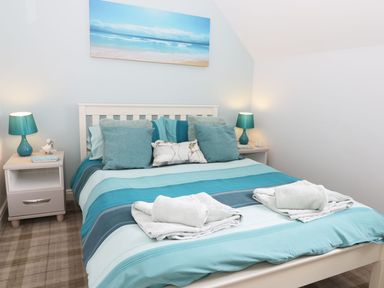 A bedroom with a bed striped blue bedding two bedside tables with blue lamps and a beach painting above the bed at Meadow View in Filey