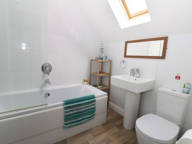 A bathroom with a bathtub a sink a toilet a wooden shelf and a skylight at Meadow View in Filey