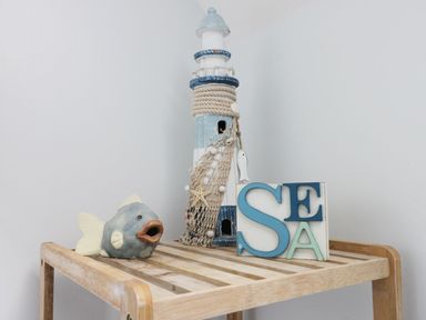 A wooden slatted table with a fish sculpture a lighthouse decoration and a sea sign