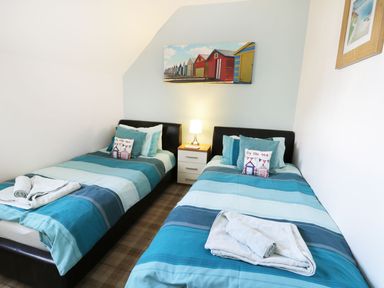 A bedroom with two single beds with blue striped bedding and a nightstand with a lamp between them at Meadow View in Filey