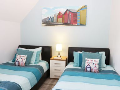 A bedroom with two single beds a bedside table with a lamp and a beach hut picture on the wall at Meadow View in Filey