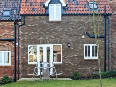 The exterior of a brick house with white framed windows and doors a small patio with chairs and a table and a lawn in front at Meadow View in Filey