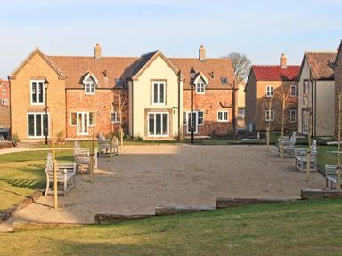 A courtyard with benches and young trees surrounded by brick and cream-colored houses at Meadow View in Filey