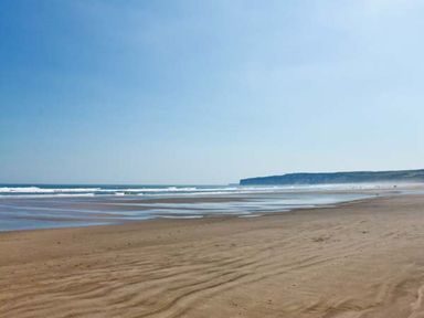 A sandy beach with waves and a distant cliff under a clear sky at Meadow View in Filey