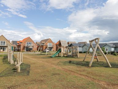 A playground with wooden play structures and swings in front of brick and blue houses at Meadow View in Filey
