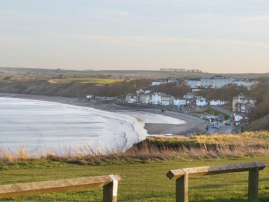 A coastal town with buildings along a shoreline and a grassy area with wooden fence in the foreground at Meadow View in Filey