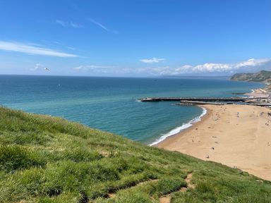 A beach with people on the sand and a jetty extending into the sea with grassy hills nearby at The Beach House in West Bay