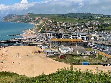 A coastal town with sandy beach harbor boats and hills in the background at The Beach House in West Bay