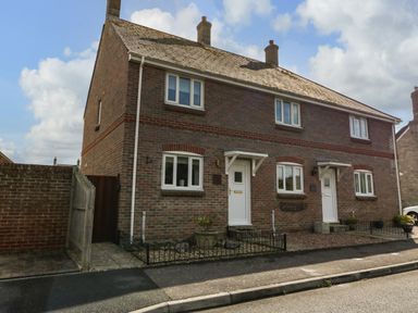 A brick semi detached house with two white front doors and small fenced garden areas at The Beach House in West Bay