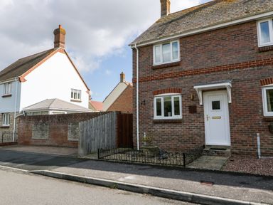 A street view of brick and white houses with a white front door and fenced front garden at The Beach House in West Bay