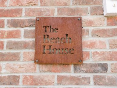 A rusted metal sign with The Beach House text mounted on a brick wall at The Beach House in West Bay