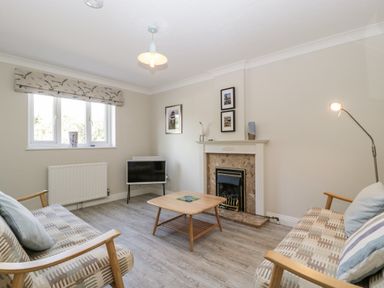 A living room with two sofas a coffee table a fireplace a floor lamp and a window at The Beach House in West Bay