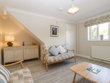 A living room with patterned sofas cushions a wooden sideboard a table lamp framed picture and a window at The Beach House in West Bay