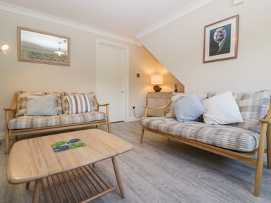 A sitting room with two wooden sofas with cushions a wooden coffee table a lamp on a cabinet and a framed picture on the wall at The Beach House in West Bay