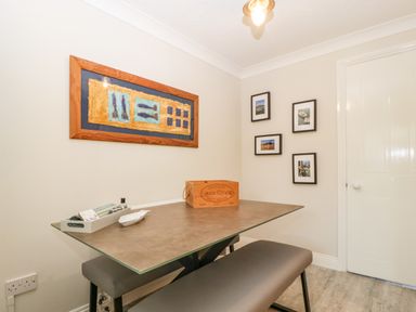 A small dining area with a bench a table and framed pictures on the wall at The Beach House in West Bay