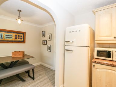 A kitchen area with a cream SMEG refrigerator a wooden cabinet and microwave a glass dining table with a grey bench and wall art at The Beach House in West Bay