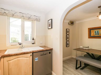 A kitchen sink with countertop dishwasher and arched doorway leading to dining area with table bench and framed pictures on wall at The Beach House in West Bay