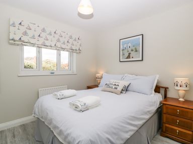 A bedroom with a bed two bedside tables and a window with sailboat patterned curtains at The Beach House in West Bay