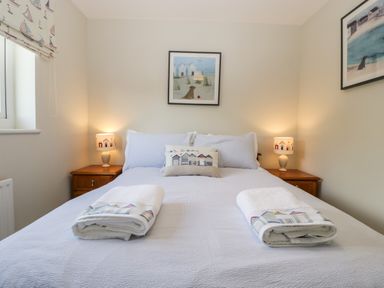 A bedroom with a made bed two bedside tables with lamps and framed pictures on the walls at The Beach House in West Bay