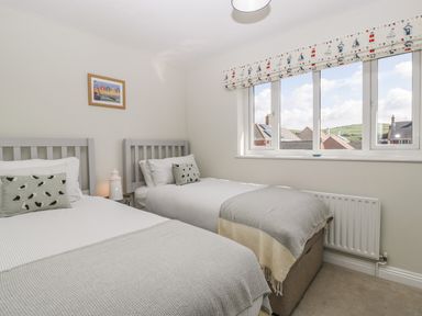A bedroom with two single beds with grey headboards and patterned cushions with a large window with patterned blinds at The Beach House in West Bay