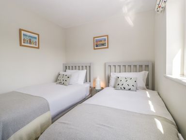 A bedroom with two single beds two framed pictures on the walls and a small round table with a lighthouse lamp between the beds at The Beach House in West Bay