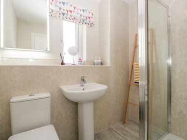 A bathroom with a toilet a pedestal sink a mirror a window with a patterned blind and a shower at The Beach House in West Bay