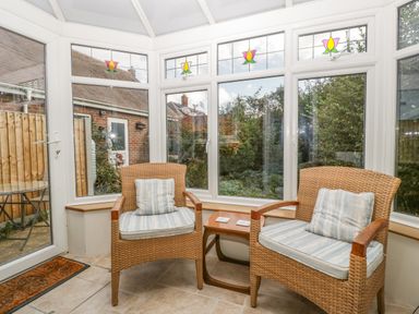 A sunroom with two wicker chairs with cushions and a small wooden side table between them at The Beach House in West Bay