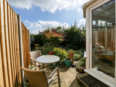 A small outdoor patio with a round table and two chairs next to a garden with plants and a wooden fence at The Beach House in West Bay